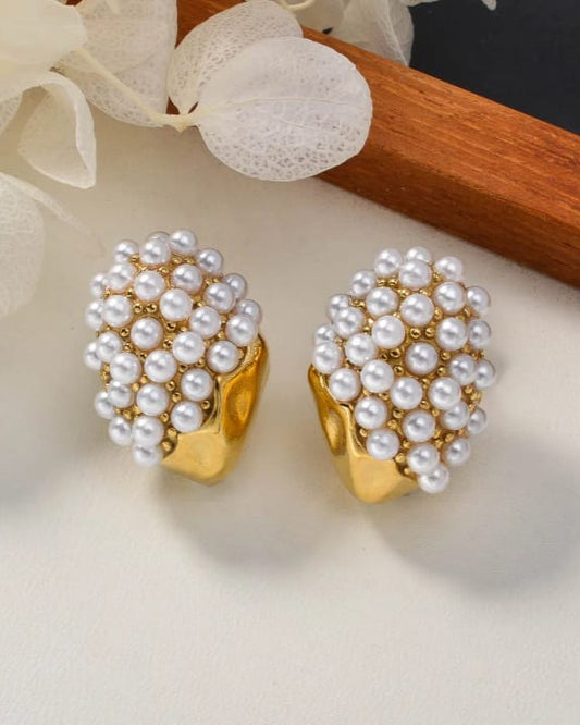 Gold earrings with pearl-like beads on a light surface with floral elements.
