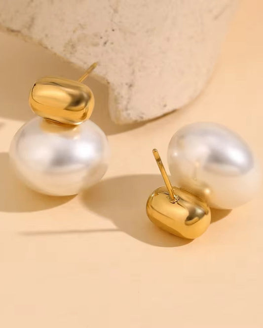 Pair of pearl and gold earrings on a beige background