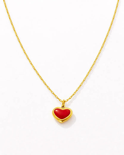 Gold necklace with a red heart pendant on a white background
