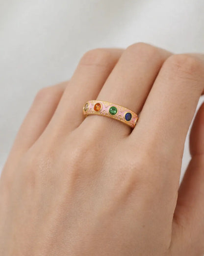 Gold ring with colorful gemstones on a hand against a neutral background