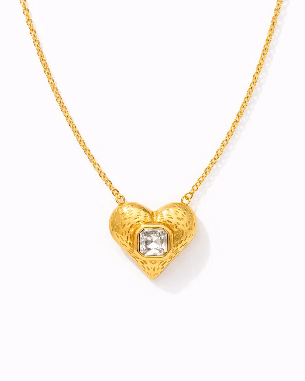 Gold heart-shaped necklace with a central gemstone on a white background