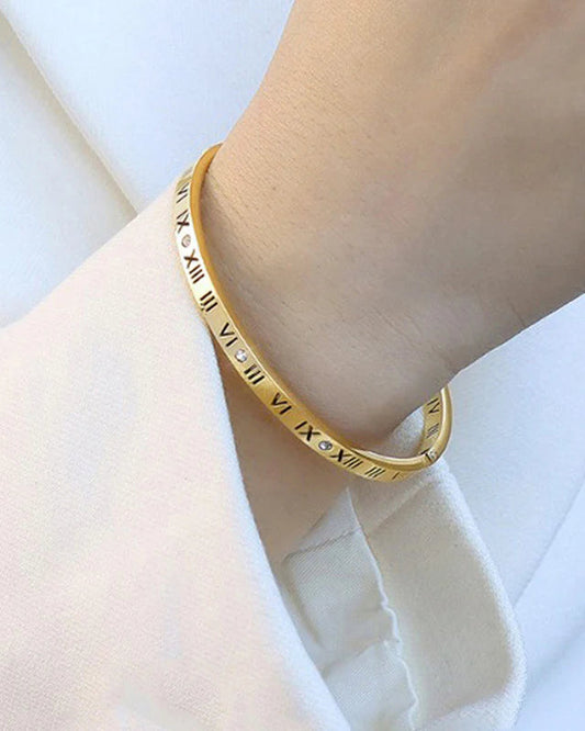 Gold bracelet with Roman numeral design on a wrist against a white background