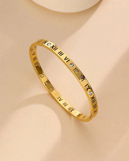 Gold bracelet with Roman numeral design on a beige background