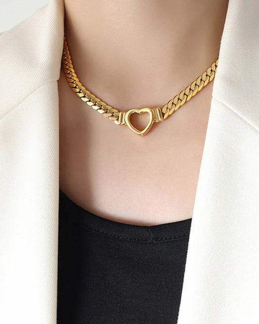 Gold chain necklace with a heart clasp worn by a person in a white blazer.