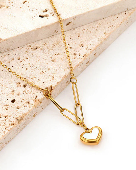 Gold necklace with a heart pendant on a light stone surface
