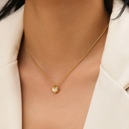 Gold necklace with a heart pendant worn by a person in a light-colored outfit.