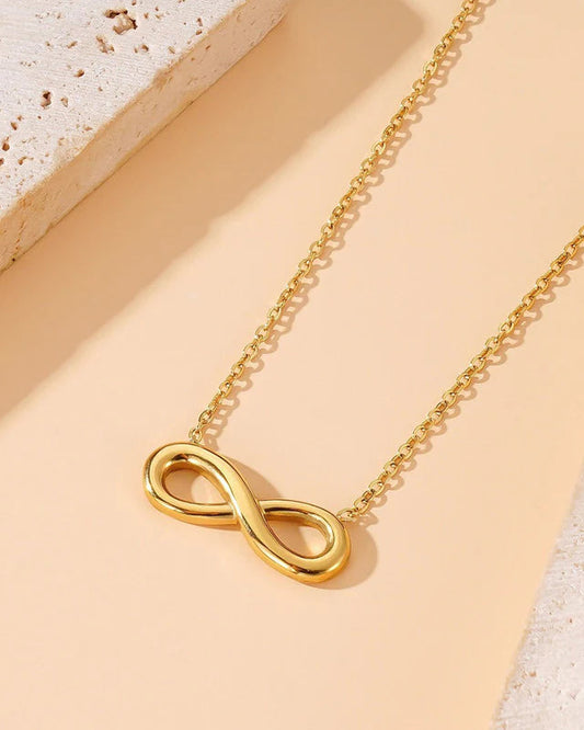 Gold infinity necklace on a beige surface