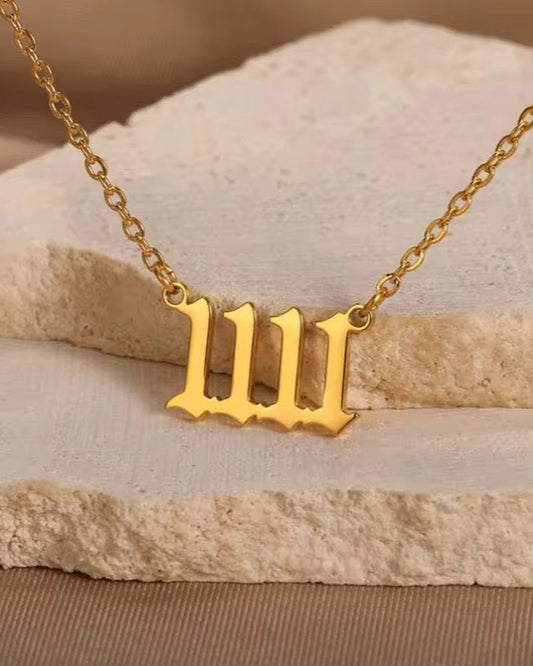 Gold necklace with a letter '1111' pendant on a stone surface