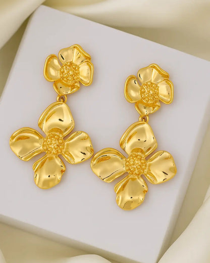Gold floral earrings on a white box with beige fabric background