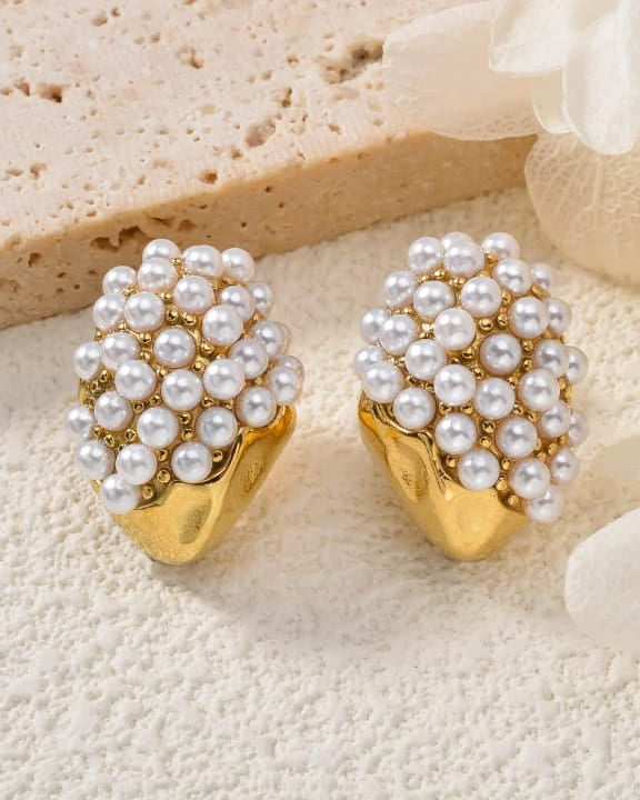 Pearl earrings with gold bases on a textured beige surface