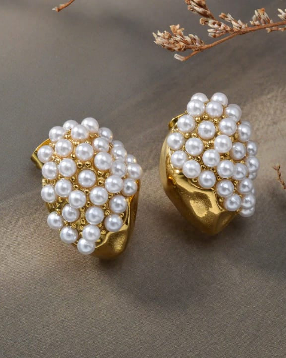 Gold earrings with pearl beads on a textured surface