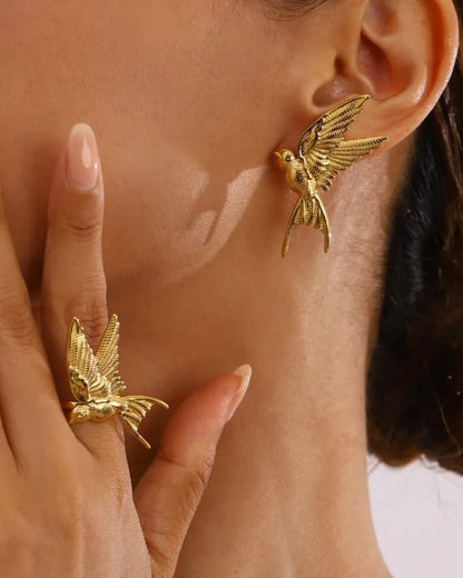 Gold bird-shaped earrings worn by a person with a hand touching their neck.