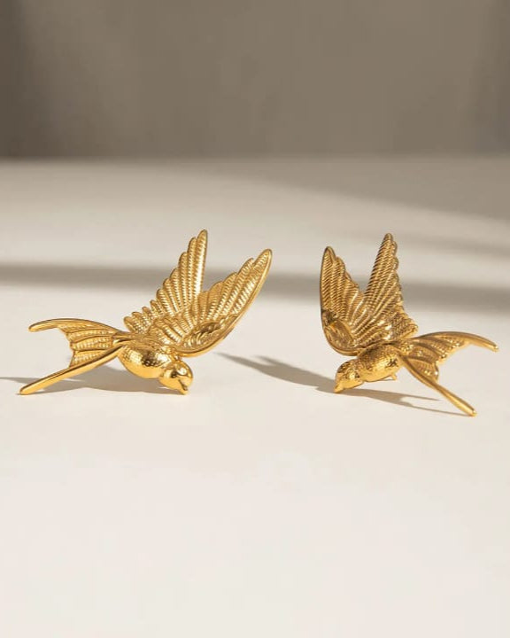 Pair of gold bird-shaped earrings on a beige background