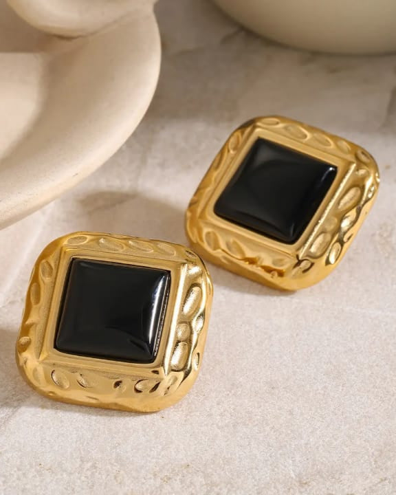 Gold square earrings with black centers on a beige surface