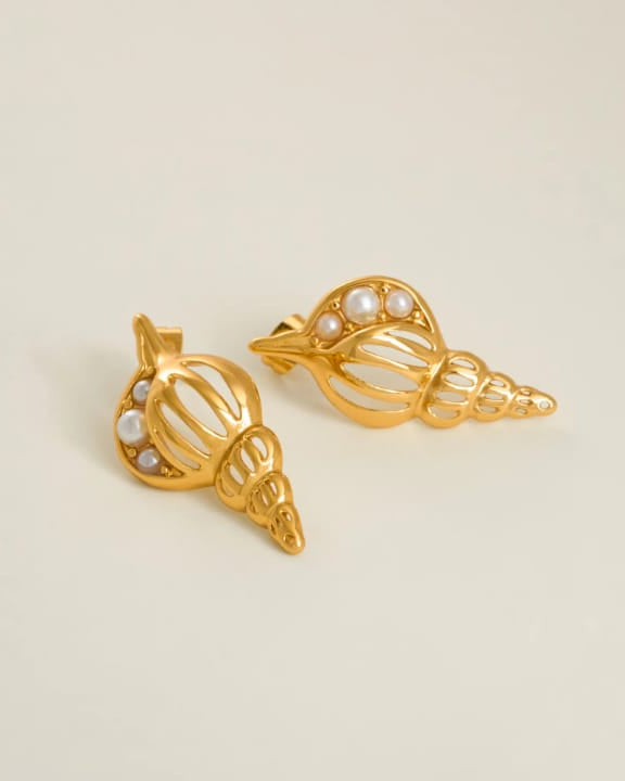 Gold shell-shaped earrings with pearl accents on a beige background