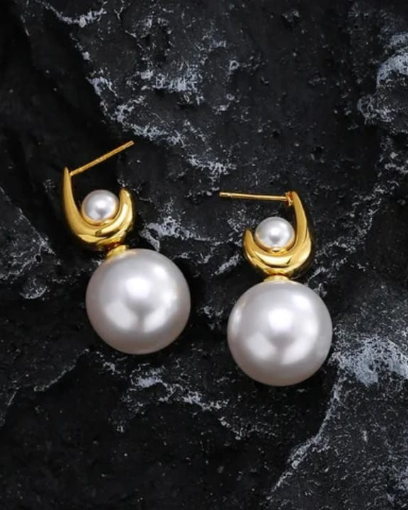 Pearl earrings with gold hooks on a dark stone surface
