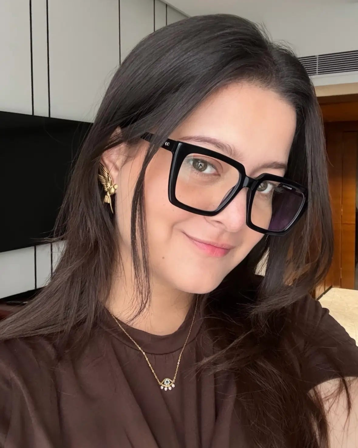 Woman wearing glasses and a brown top indoors