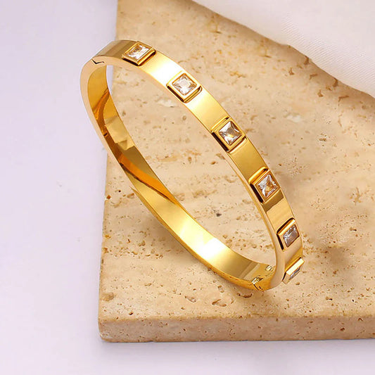 Gold bracelet with embedded stones on a beige stone surface