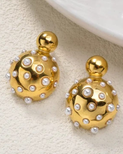 Gold earrings with pearl accents on a textured beige surface